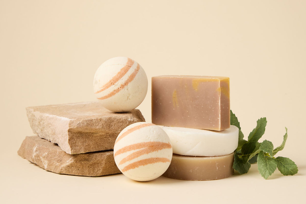 Milk & Honey Bath Set: striped bath bombs and bars of soap stacked on stone slabs beside fresh mint