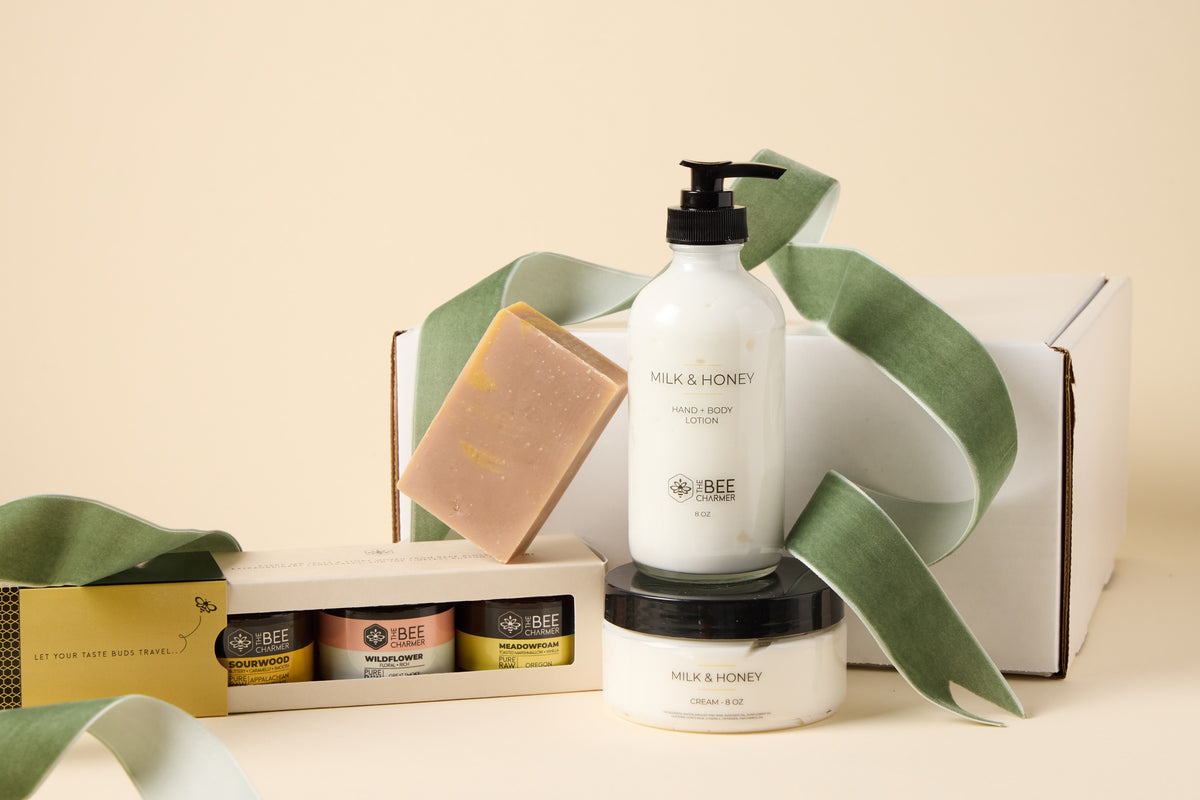 Honey & Body Care Gift Set: three jars of raw honey in a gift box with Milk and Honey bar soap, lotion and cream, shown with a green ribbon beside a white shipping box